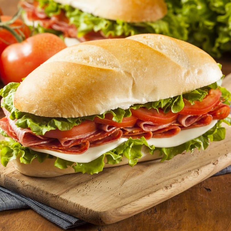 A delicious Pietro's Pizza sub sandwich with salami, cheese, lettuce, and tomatoes on a wooden board.