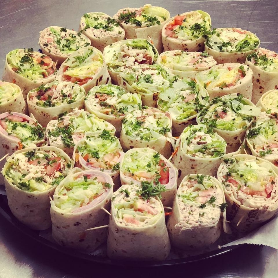 A platter of various wraps, some with ham and cheese, others with tuna salad.