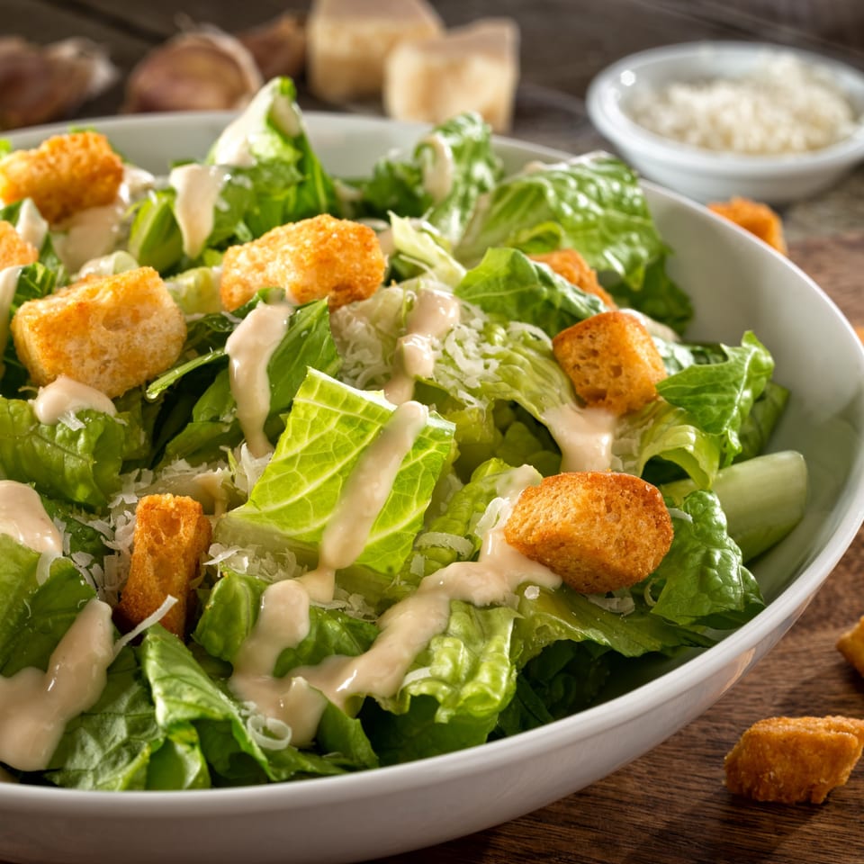 A close-up of a Caesar salad with romaine lettuce, croutons, parmesan cheese, and dressing.