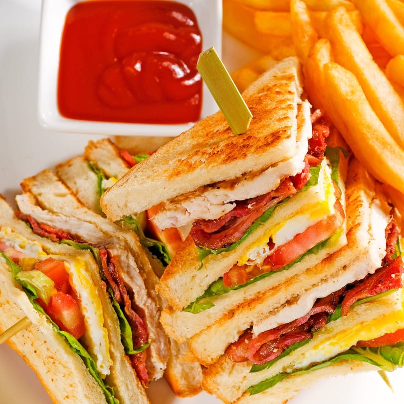 Club sandwiches with bacon, egg, lettuce, and tomato, served with fries and ketchup.