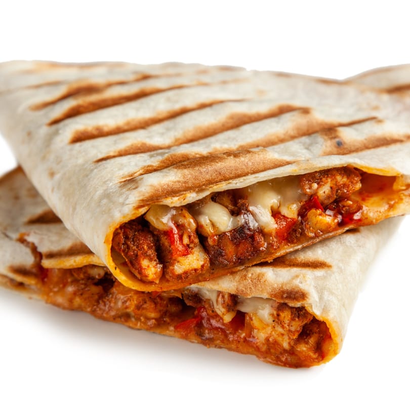 Two grilled chicken quesadillas with melted cheese and red sauce, stacked on a white background.