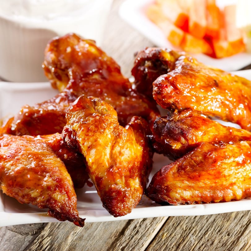 Close-up of a plate of glistening, saucy chicken wings, with a white dipping sauce in the background.